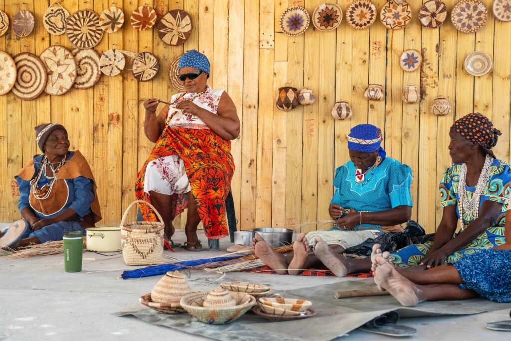 Immersion à Khwai : quatre artisanes en plein travail, entourées de paniers tressés traditionnels.