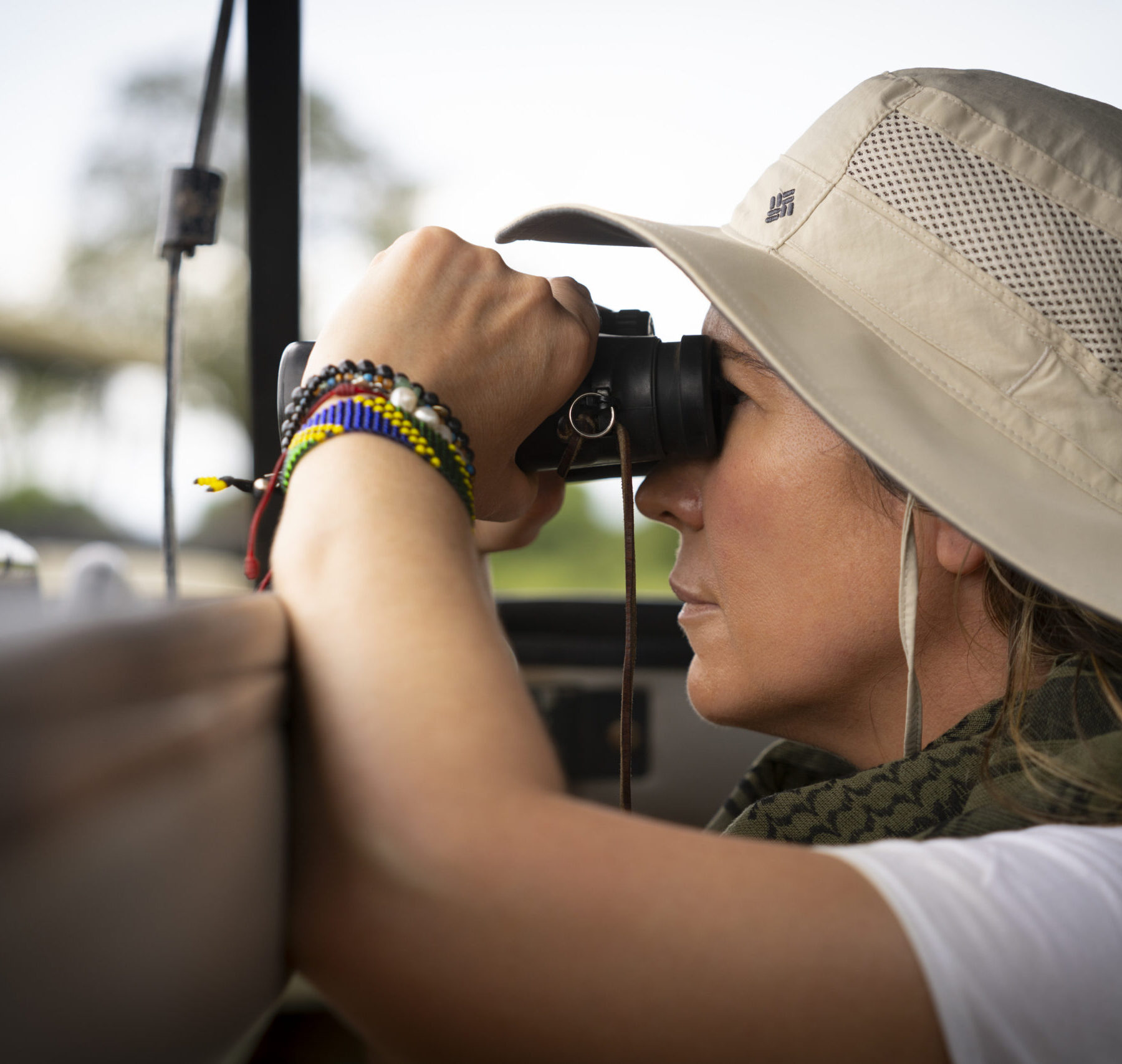 Woman with a hat and binoculars looking out from a car in Serengeti