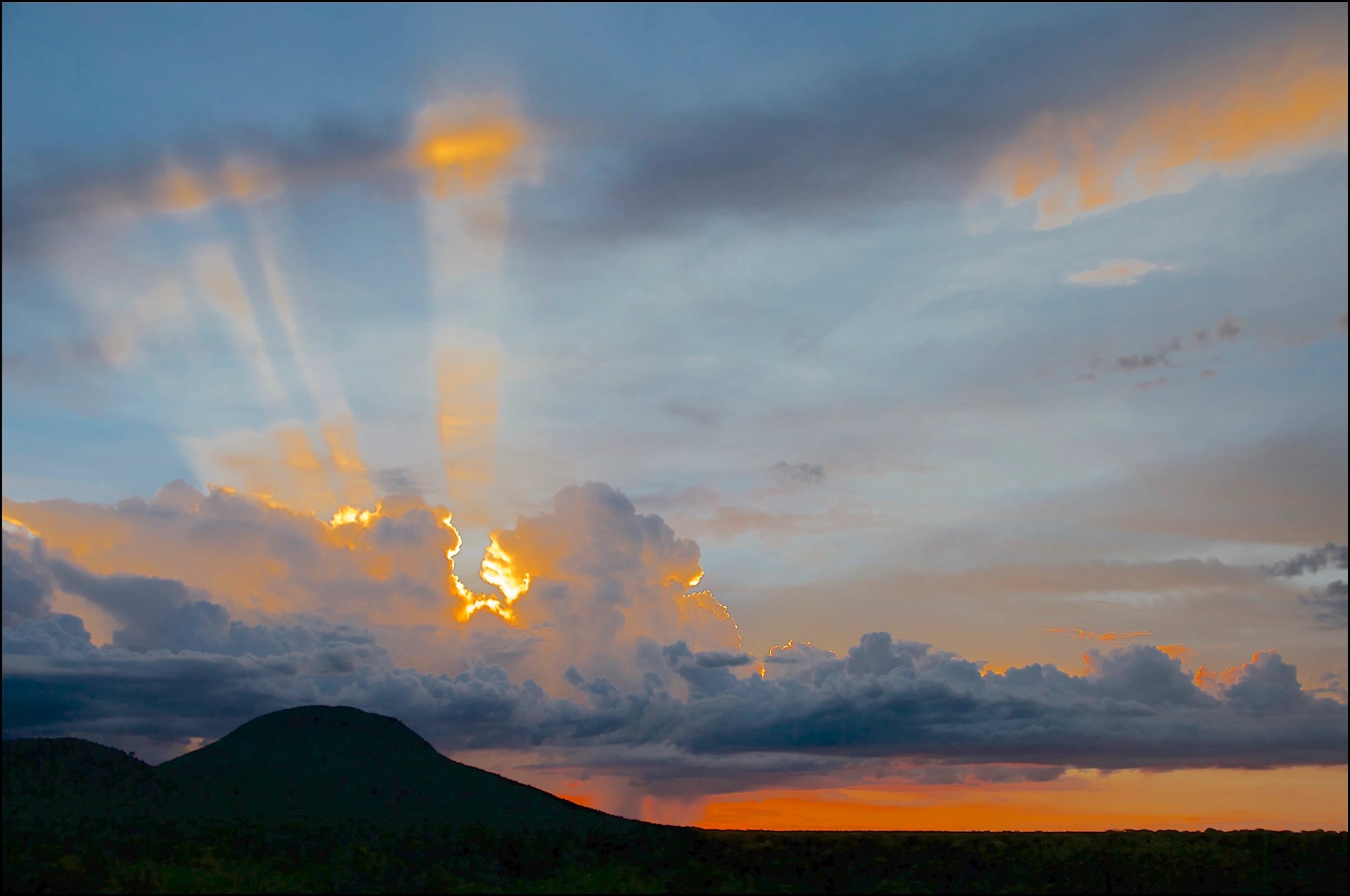 Nuages sombres au-dessus de la réserve naturelle d'Okonjima en Namibie, avec des montagnes au premier plan et le soleil traversant les nuages.